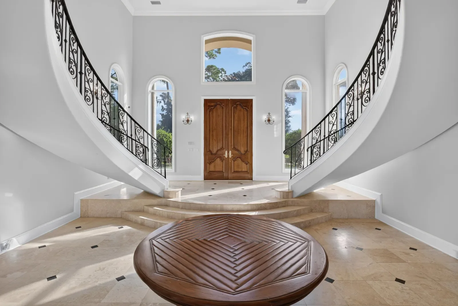 Marble rotunda with twin curved staircases and carved front doors in Jacksonville, FL. Real estate photography by Megapixeler