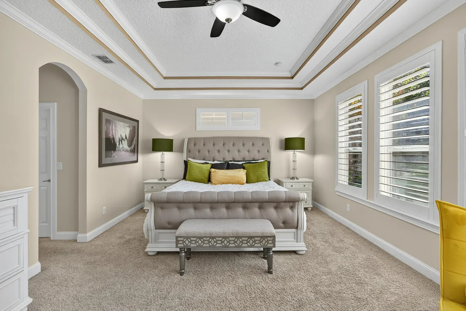 Primary bedroom with tufted bed and plantation shutters in Fruit Cove, FL. Real estate photography by Megapixeler