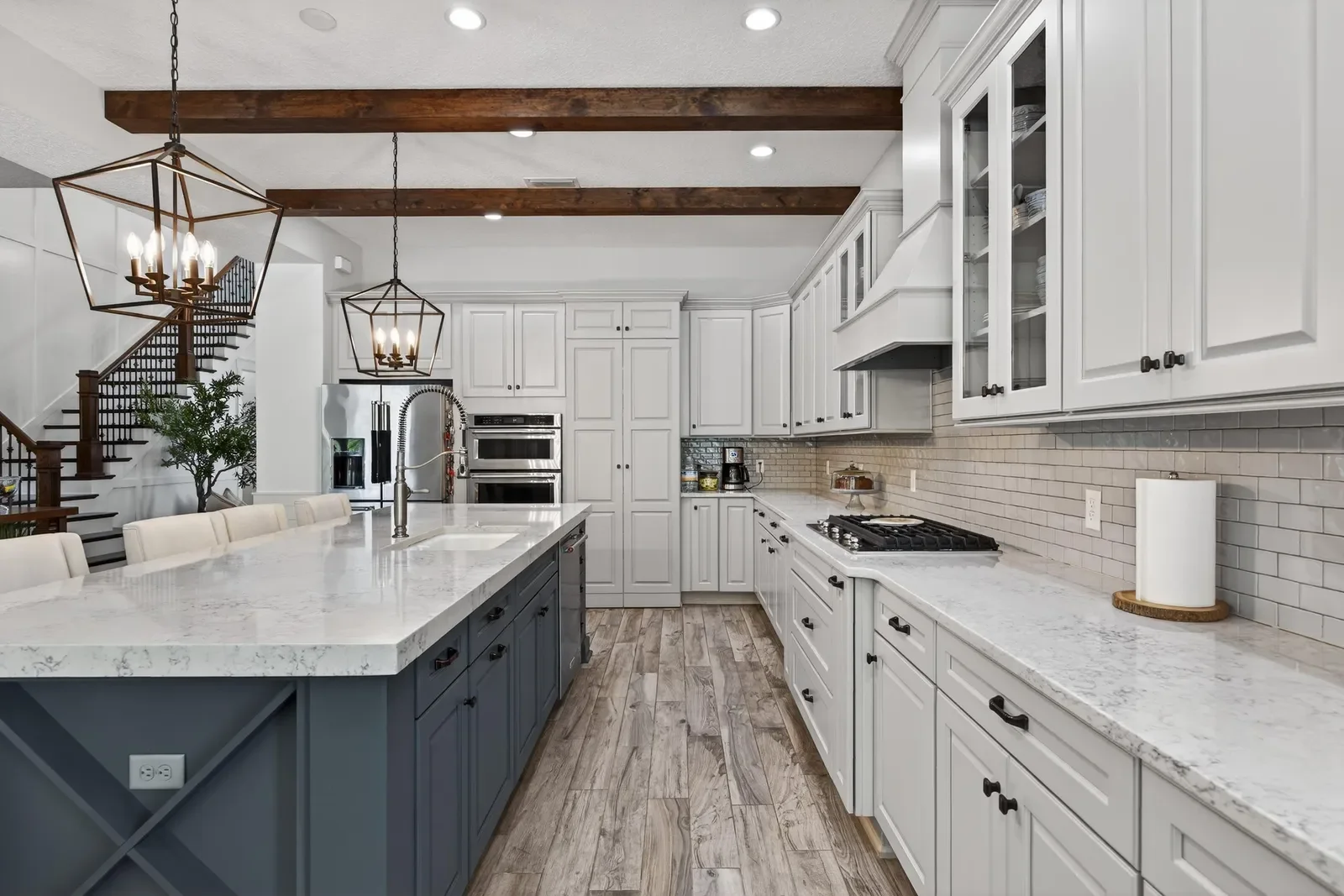 White kitchen with marble island, subway tile and staircase view in St. Johns, FL. Real estate photography by Megapixeler